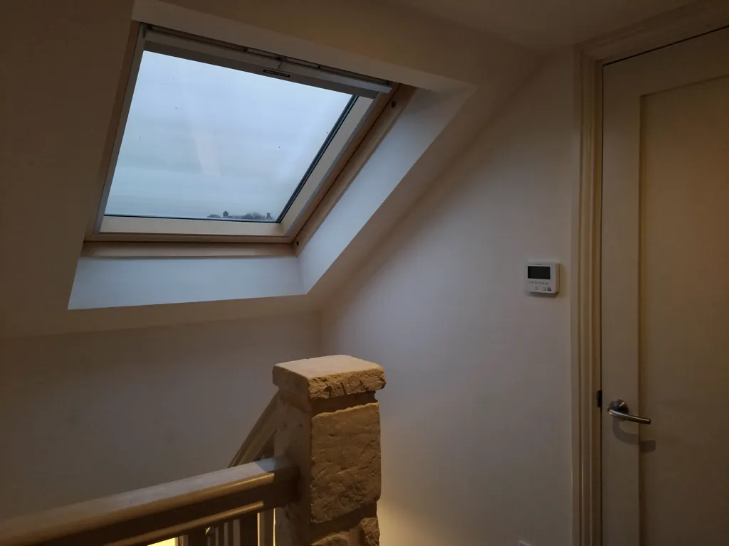 An electric rooflight closed above a landing at dusk, the work finished