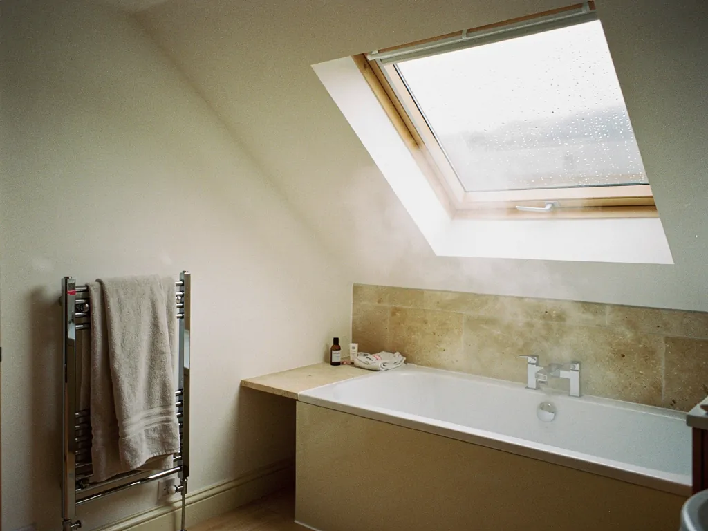 A bathroom with a roof window open above the bath