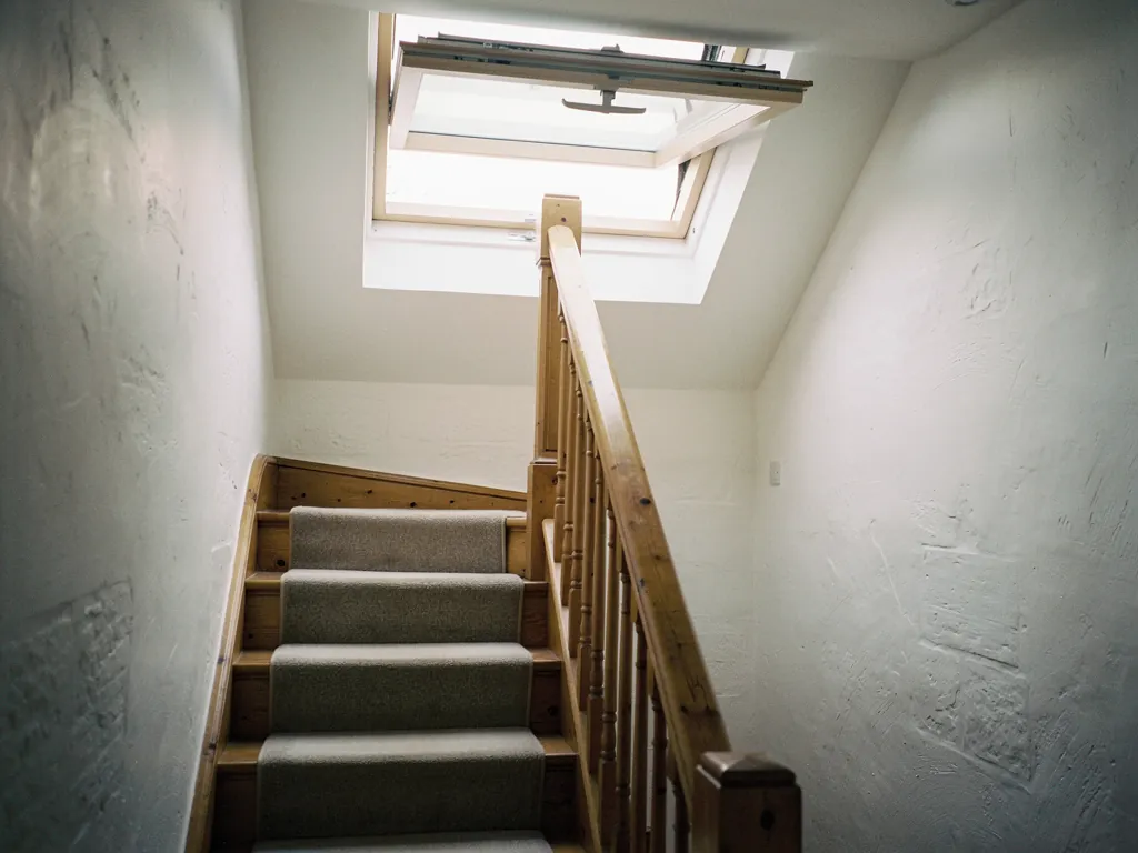 A narrow terraced-house stairwell lit by an open roof window at the top